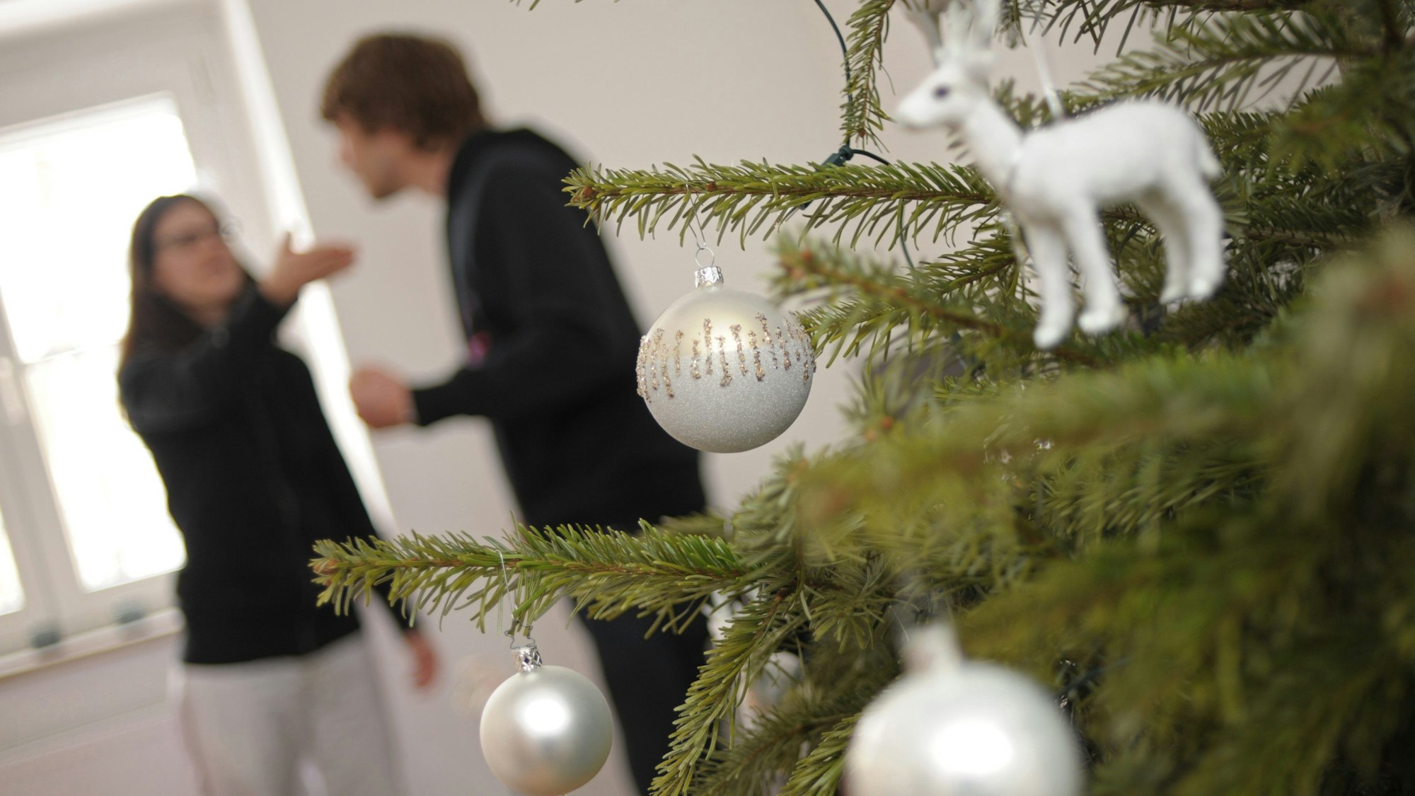 Ein Pärchen streitet sich am hinter einem geschmückten Christbaum.