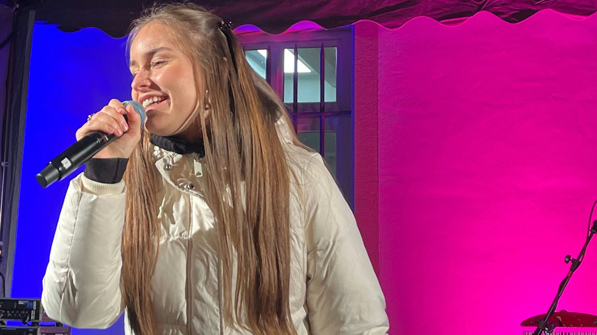 Eine junge Frau steht mit einem Mikrofon auf einer beleuchteten Bühne.