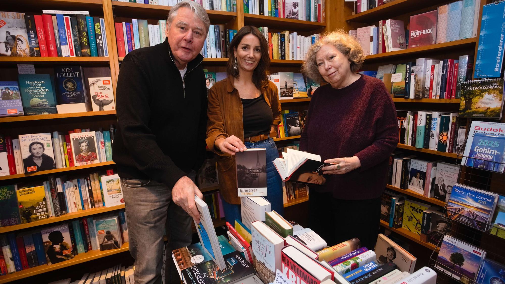 Das Foto zeigt drei Personen vor Bücherregalen.