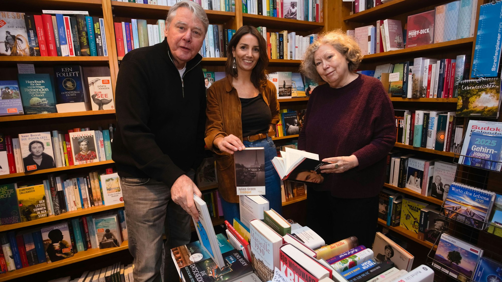Das Foto zeigt drei Personen vor Bücherregalen.