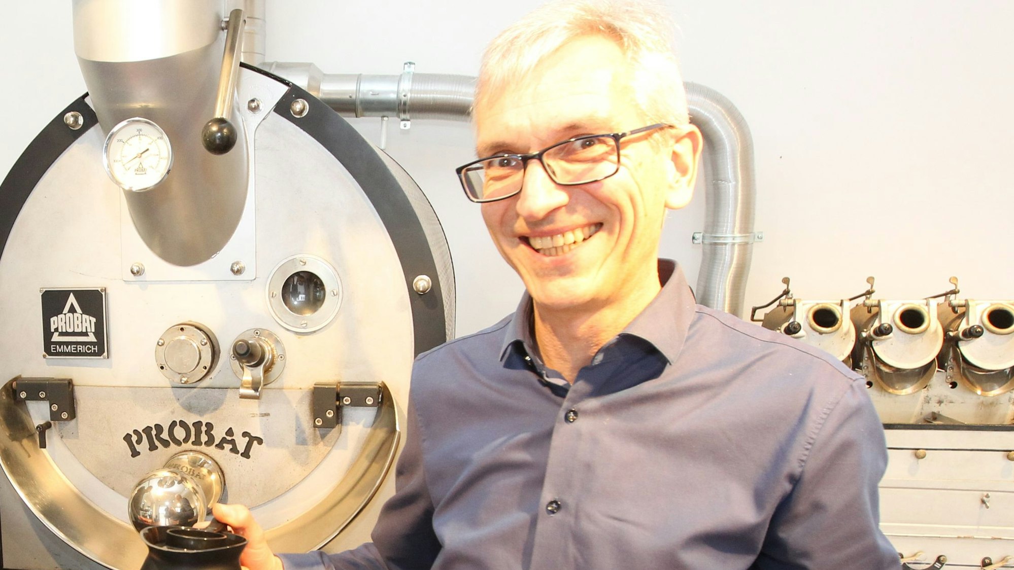 Ein Mann steht vor einer Rösttrommel für Kaffee.