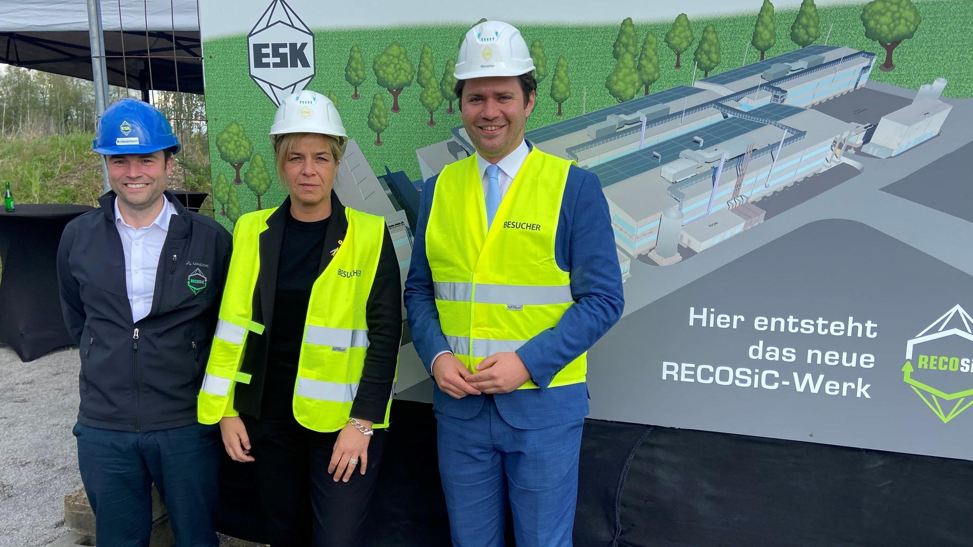 Auf dem Bild sind drei Personen zu sehen, die eine Baustelle besichtigen.