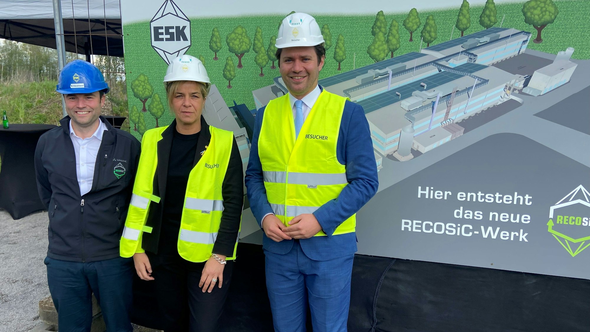 Auf dem Bild sind drei Personen zu sehen, die eine Baustelle besichtigen.