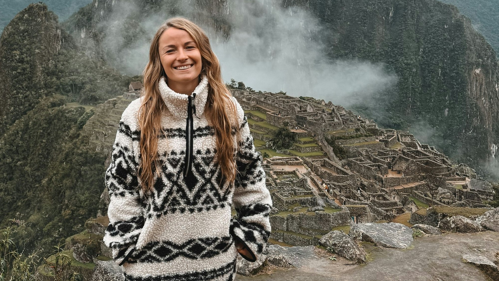 Jil Eileen Füngeling steht auf einer Anhöhe, im Hintergrund ist die Ruinenstadt Machu Picchu zu sehen.