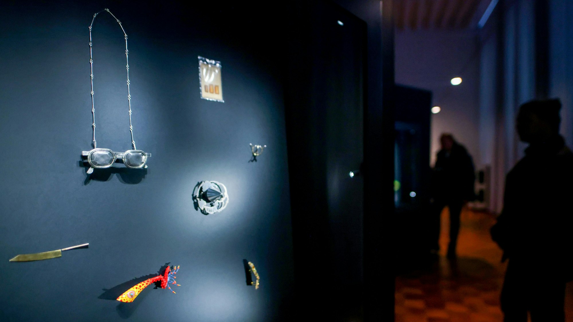 Das Bild zeigt eine erleuchtete Vitrine mit modernen Schmuckobjekten in den abgedunkelten Räumen des Museums für Angewandte Kunst in Köln.