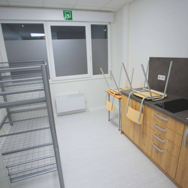 Innenansicht eines Containers für Geflüchtete – mit Küchenzeile, Hochbett, einem Tisch und zwei Stühlen.