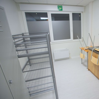 Innenansicht eines Containers für Geflüchtete – mit Küchenzeile, Hochbett, einem Tisch und zwei Stühlen.