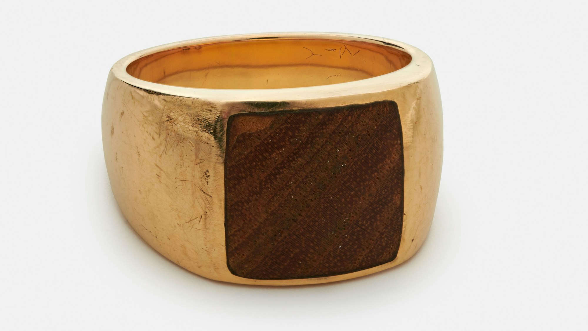Ein voluminöser goldener Ring, in den ein quadratisches Stück Holz einer Tischplatte eingfasst ist.