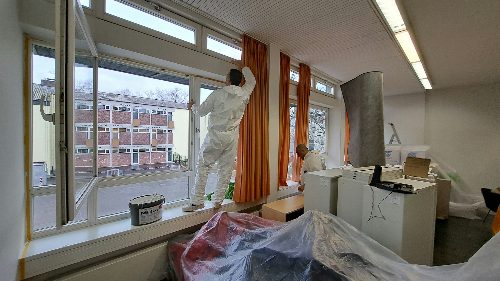Zwei Männer tragen weiße Maleranzüge und streichen ein Klassenzimmer.