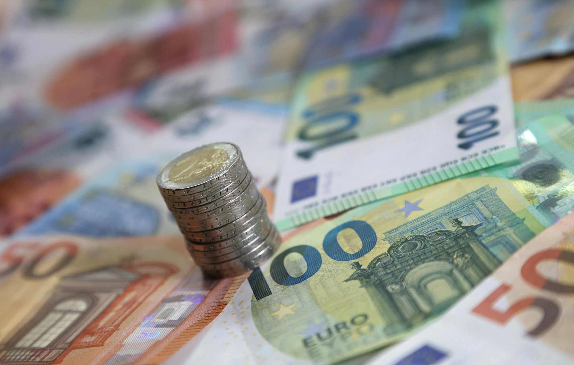 Ein Stapel mit Zwei-Euro-Münzen steht auf verschiedenen Euro-Banknoten.