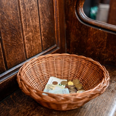 Ein Korb mit der Kollekte aus Geldscheinen und Münzen steht auf einer Kirchenbank (Symbolbild).