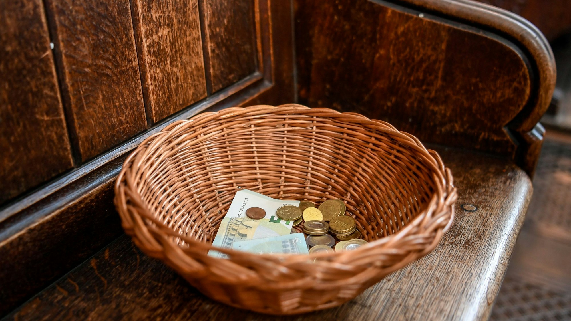 Ein Korb mit der Kollekte aus Geldscheinen und Münzen steht auf einer Kirchenbank (Symbolbild).