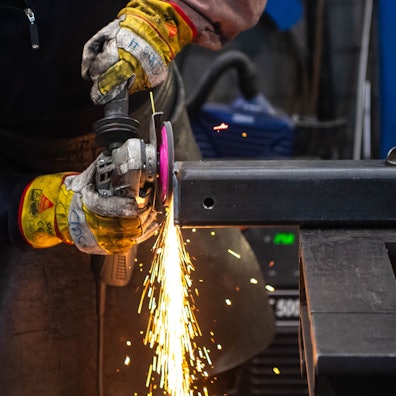 Das Bild zeigt einen Metallbauer, der eine Metallkonstruktion abschleift.