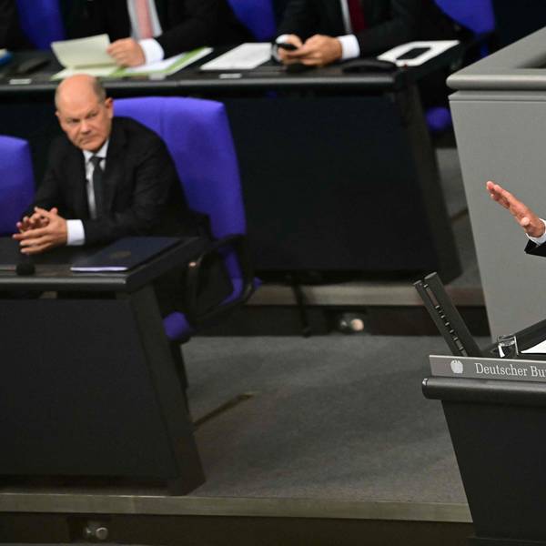 Friedrich Merz hält eine Rede im Bundestag, während Olaf Scholz ihm von der Regierungsbank aus zuschaut.