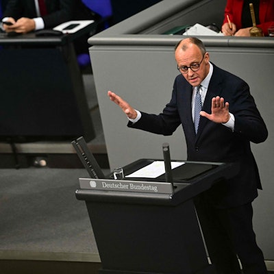 Friedrich Merz hält eine Rede im Bundestag, während Olaf Scholz ihm von der Regierungsbank aus zuschaut.