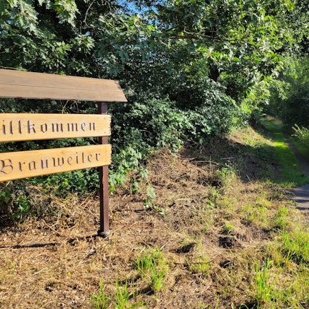 Ein Willkommensschild aus Holz begrüßt Einheimische und Zugereiste in Brauweiler.