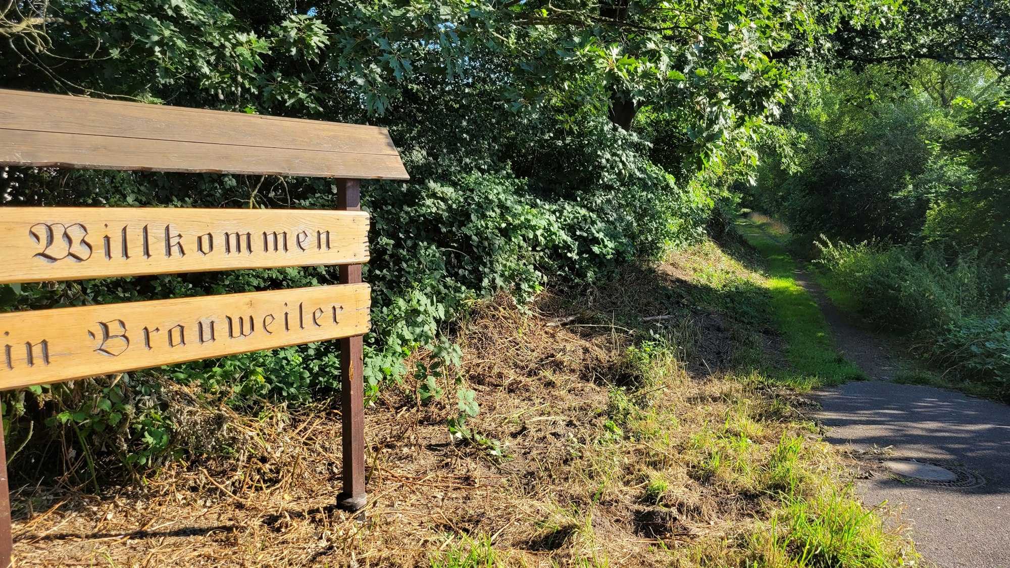 Ein Willkommensschild aus Holz begrüßt Einheimische und Zugereiste in Brauweiler.