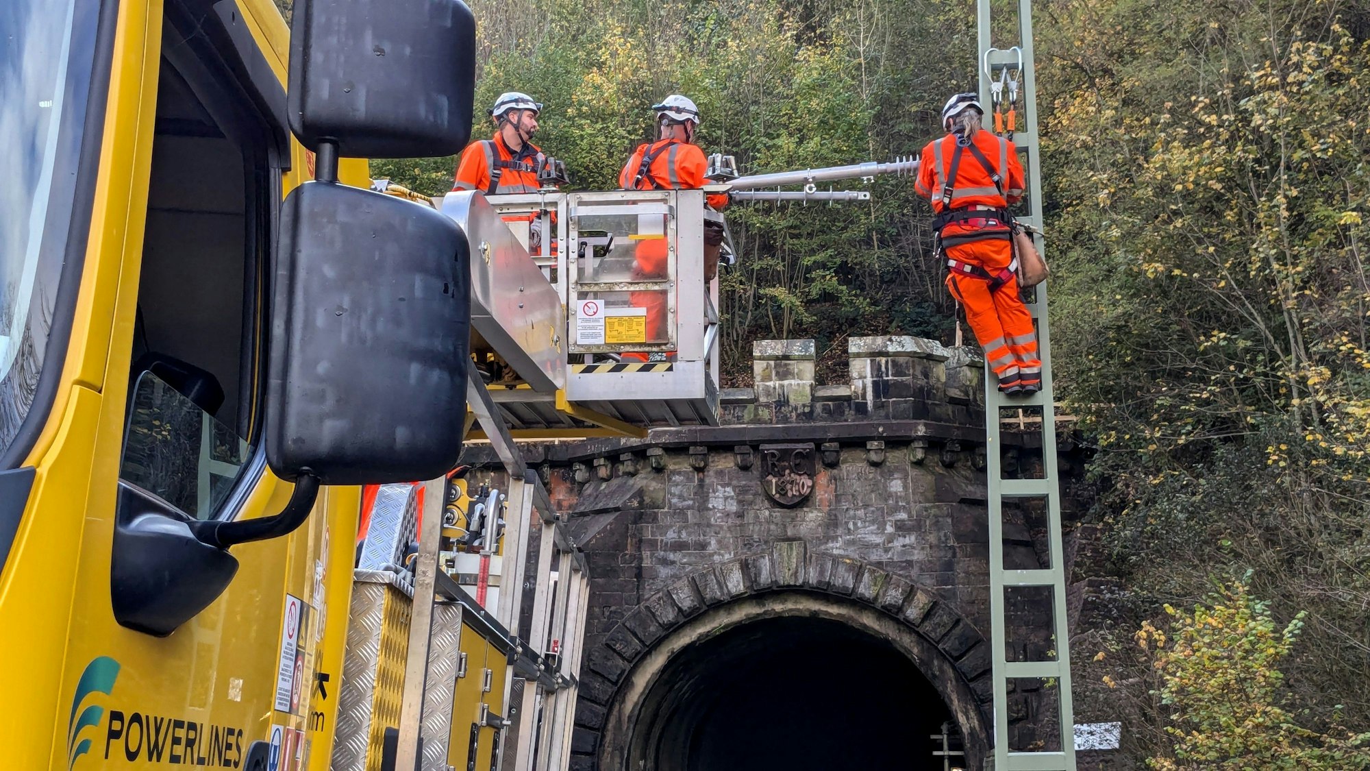 Bahnarbeiter demonstrieren die Montage eines Flachmasts mit angelenktem Ausleger am Eingang zum Wilsecker Tunnel bei Kyllburg.
