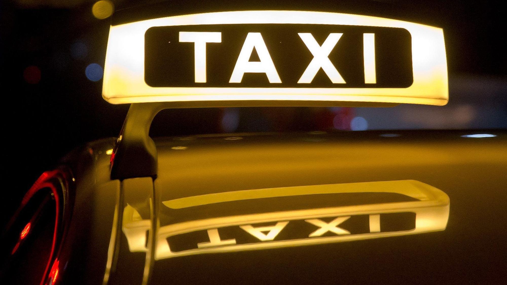 Ein Taxi steht mit leuchtendem „Taxi“-Schild für Fahrgäste bereit.