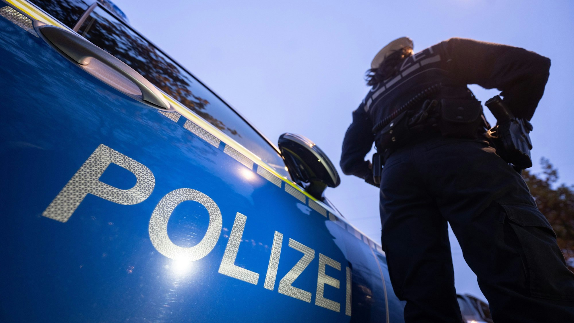 Eine Polizistin steht neben einem Polizeifahrzeug.