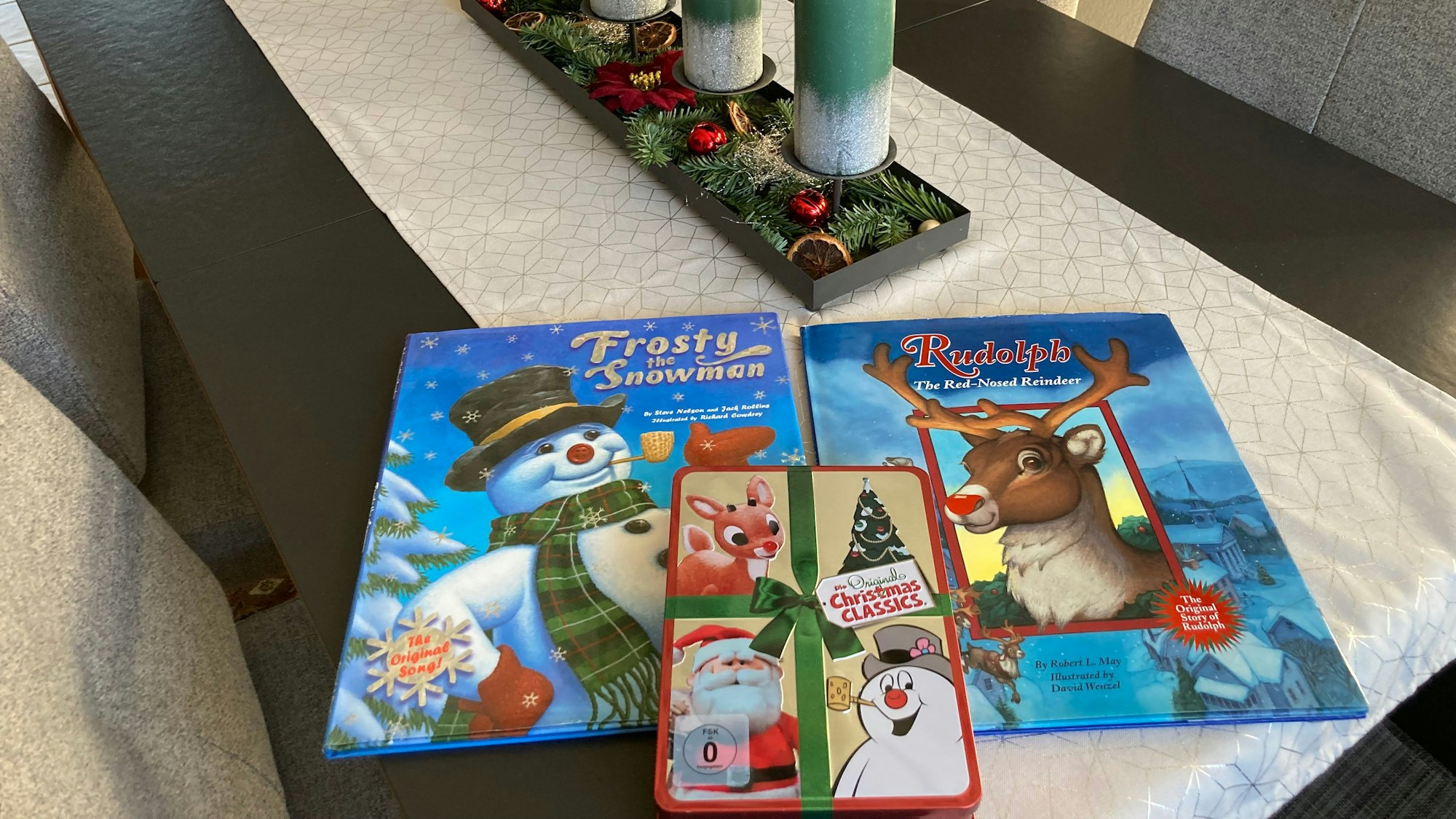 Mehrere Kinderbücher liegen auf einem Tisch mit einem Adventsgesteck.