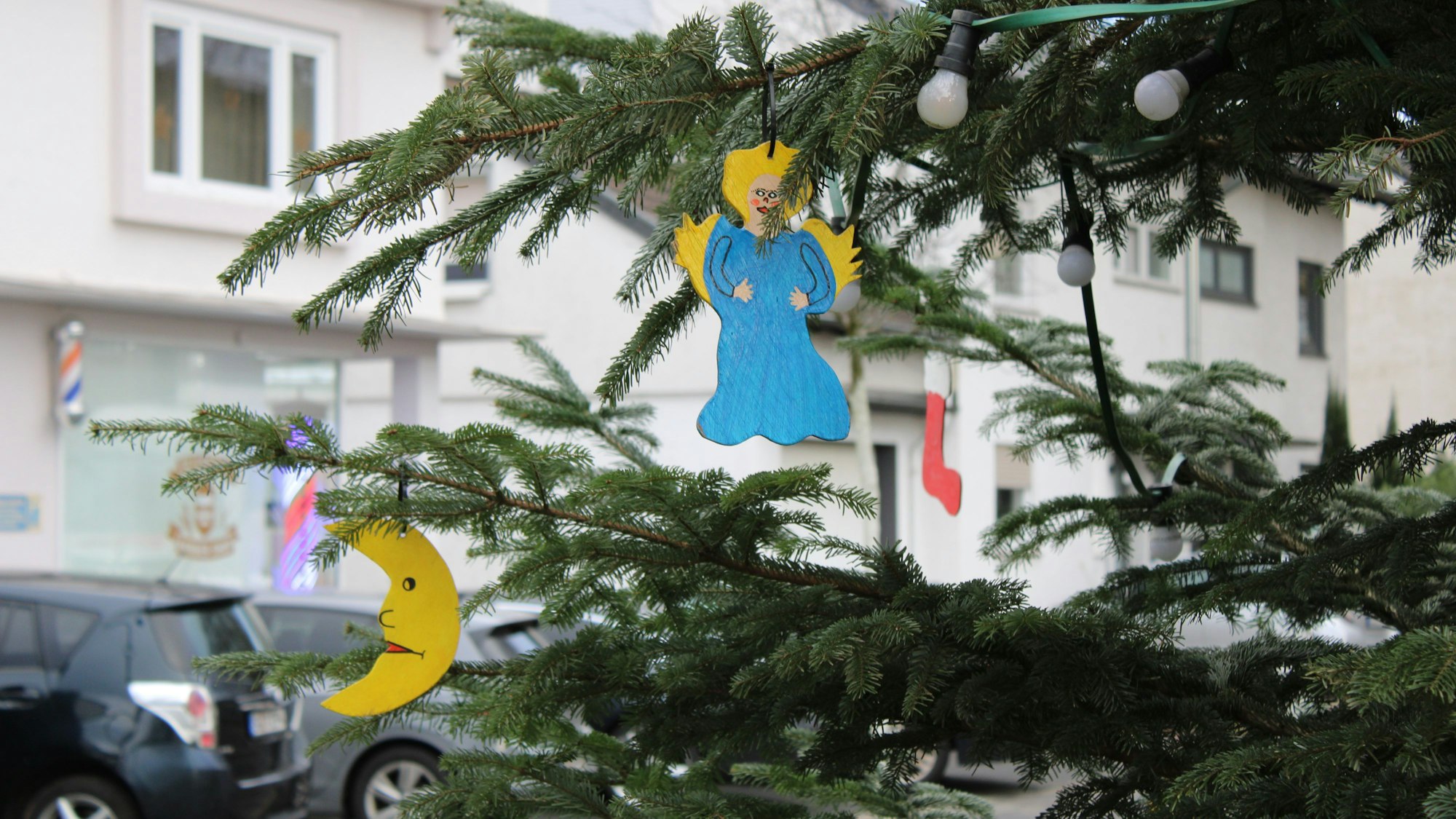Ein Engel und ein Halbmond hängen an einem geschmückten Tannenbaum im Freien.