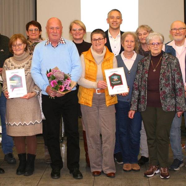 17 Männer und Frauen stehen für ein Gruppenfoto zusammen, in der vorderen Reihe werden Blumensträuße und Urkunden gehalten.