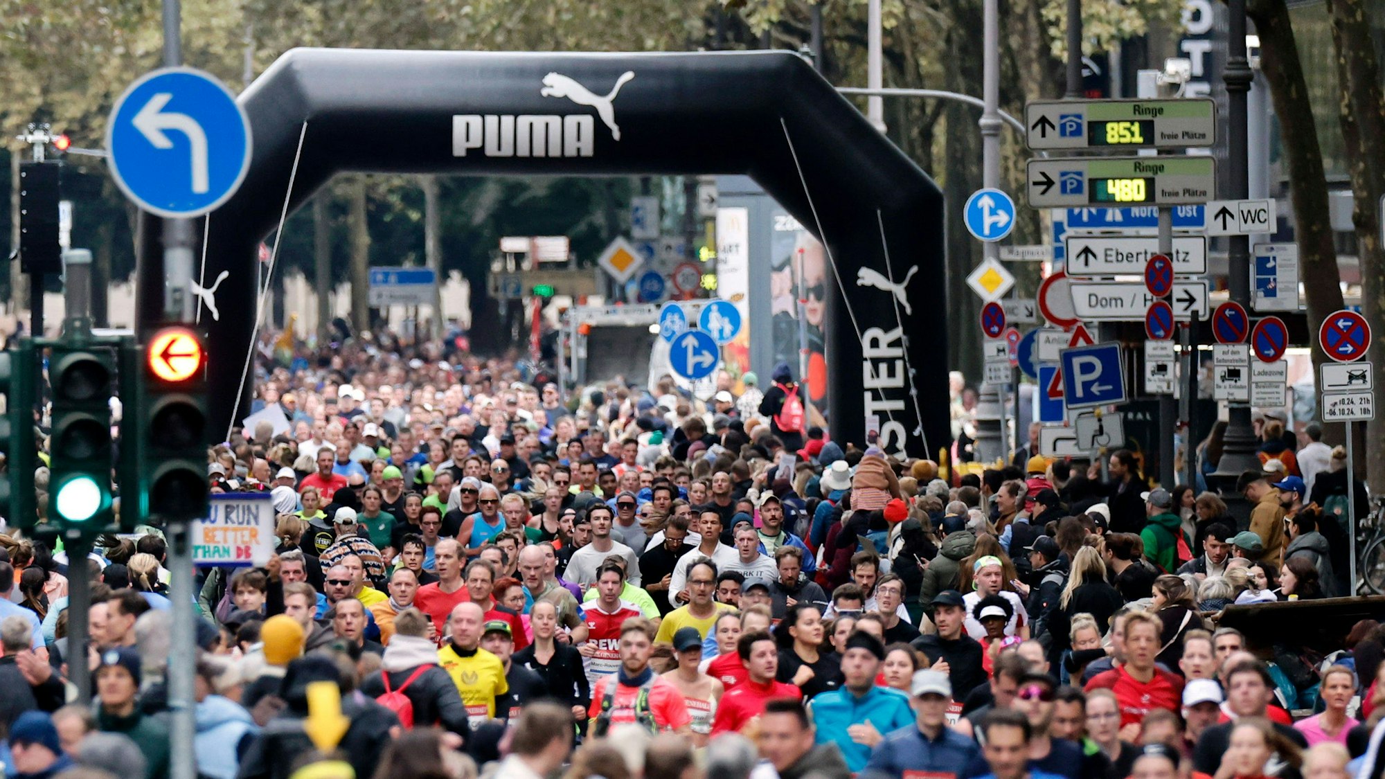 Teilnehmer beim 26. Generali Köln Marathon 2024 laufen durch die Kölner Innenstadt. Zahlreiche Zuschauer feuern die Läufer mit selbstgebastelten Plakaten an.