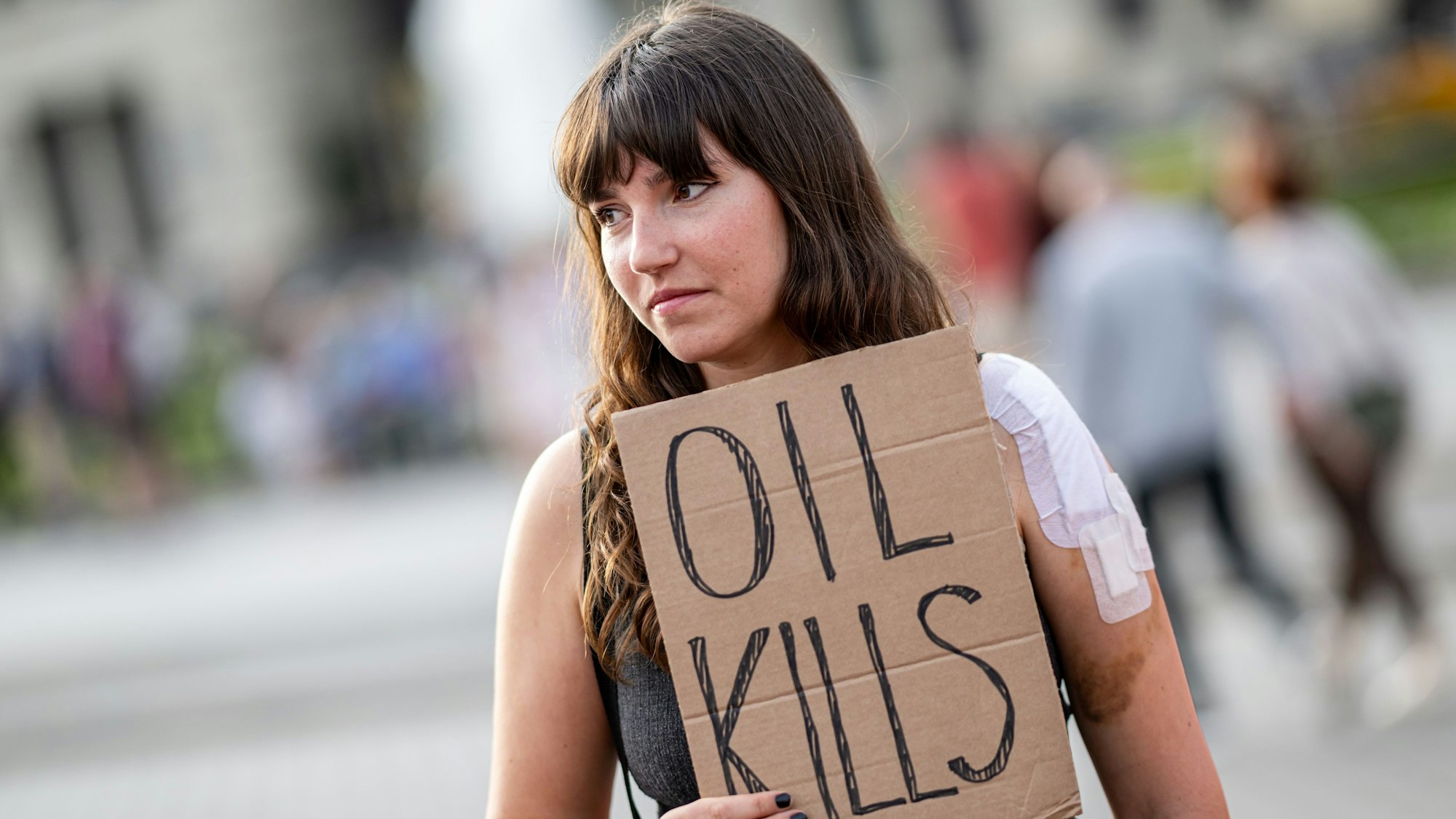 Das Bild zeigt Carla Hinrichs, Klimaschutzaktivistin, die an einer Versammlung der Letzten Generation als Reaktion auf deine Hausdurchsuchungen der Polizei vor dem Brandenburger Tor teilnimmt. Sie hält ein Schild mit der Aufschrift „Oil kills“ in der Hand. Foto: Fabian Sommer/dpa