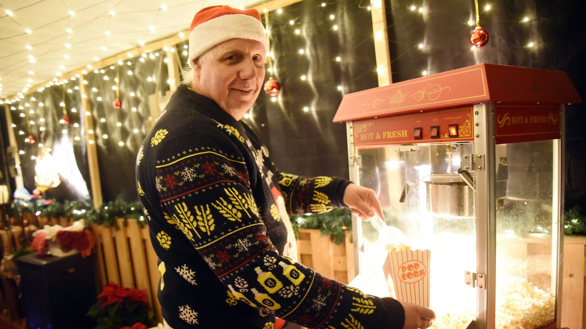 Ralf Haase füllt Popcorn in eine Tüte. Er trägt eine Nikolausmütze und einen Weihnachtspullover.