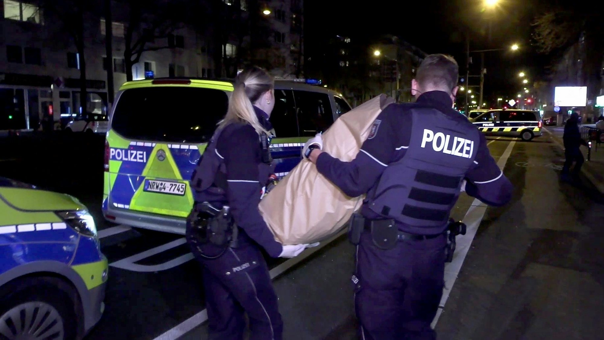 Einsatzkräfte der Polizeikräfte tragen den Koffer weg, der am Mittwochabend einen Großeinsatz im Rewe am Barbarossaplatz auslöste.