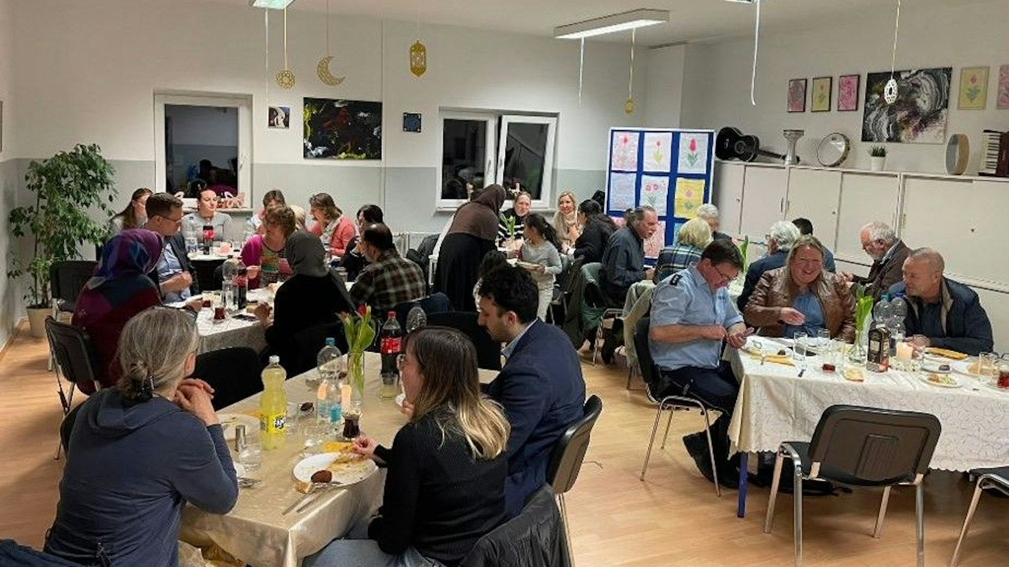 Ca. 25 Menschen sitzen gemeinsam an Tischen und essen.
