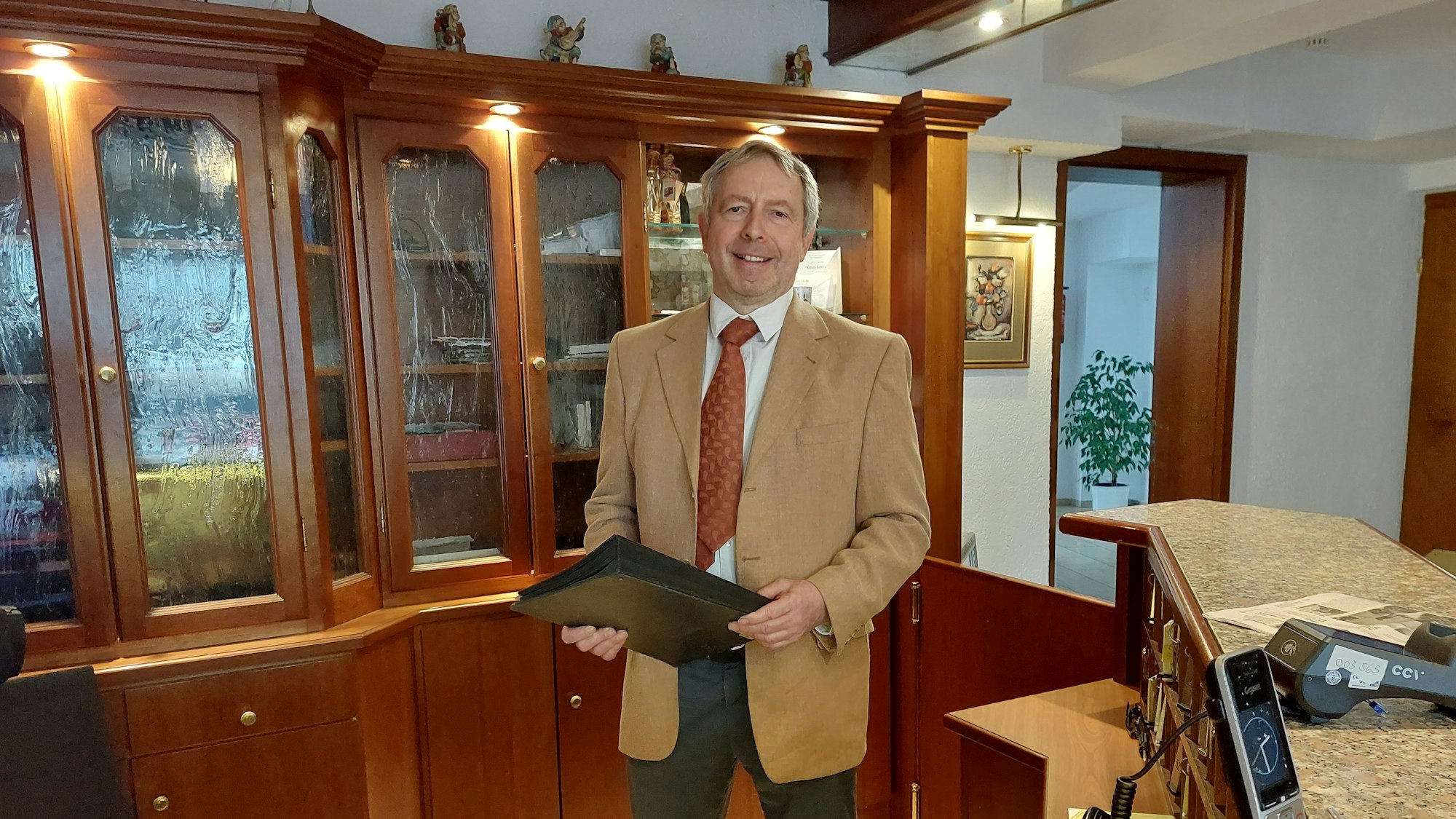 Ein Mann mit Krawatte und hellem Sakko steht am Empfang eines Hotels.