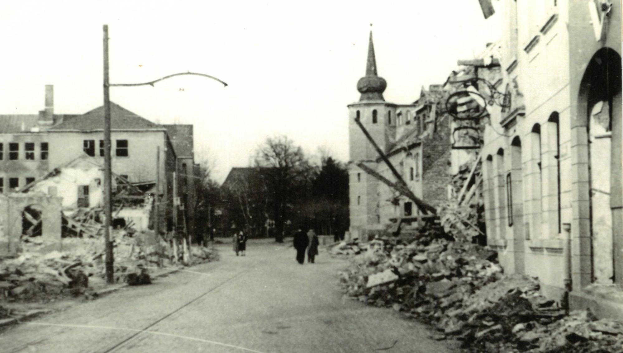 Trümmerteile von bombardierten Häusern liegen an einem Straßenrand.