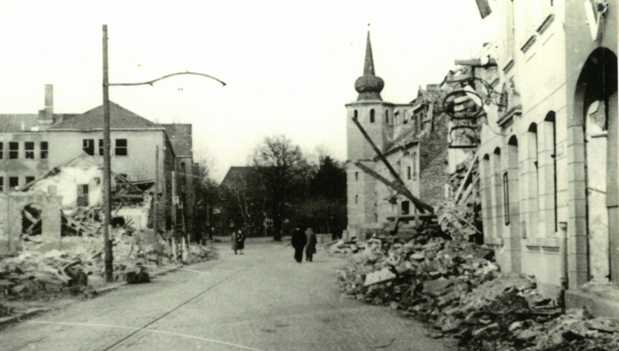 Trümmerteile von bombardierten Häusern liegen an einem Straßenrand.
