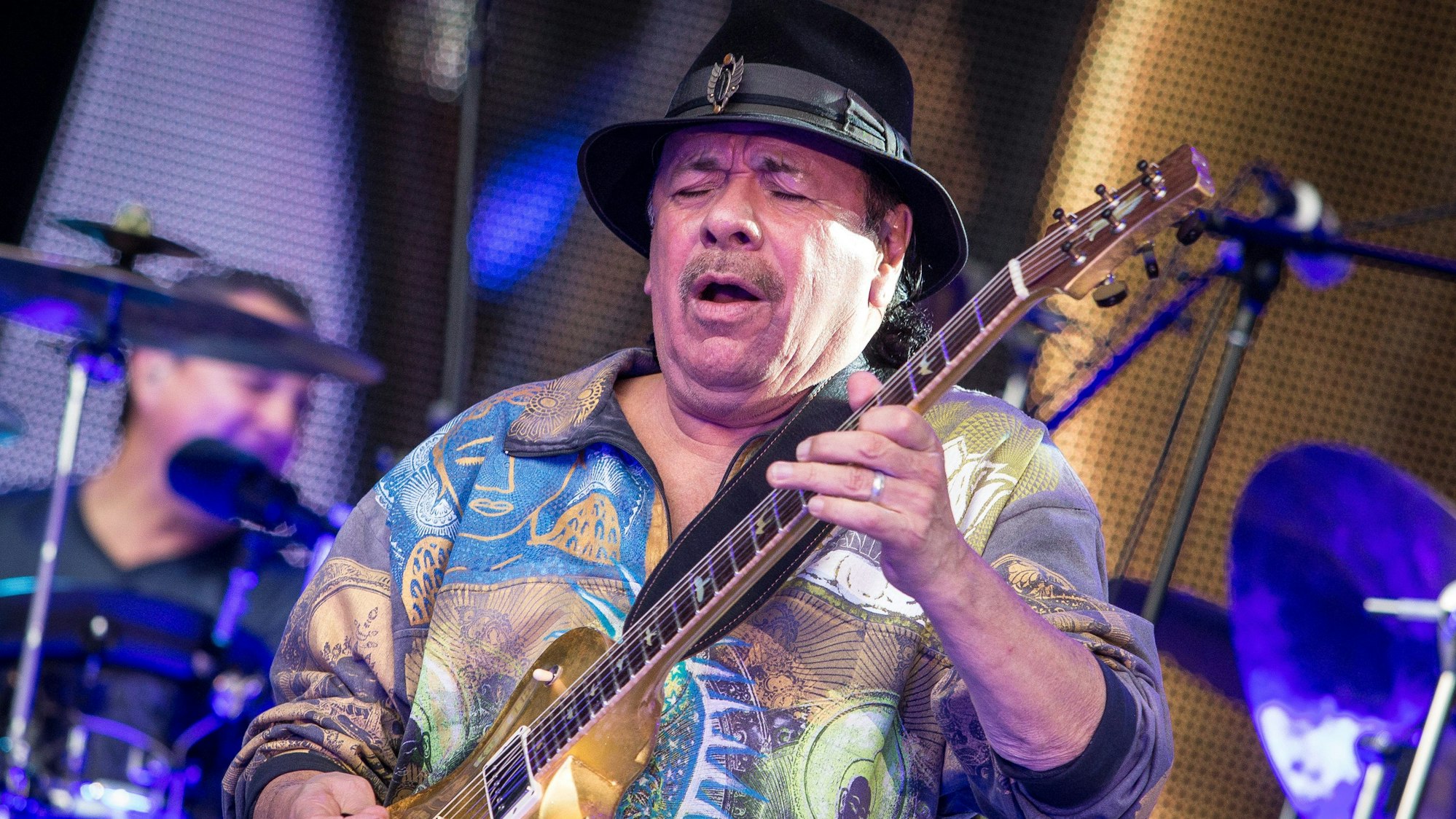 Carlos Santana steht auf einer Bühne und spielt Gitarre.