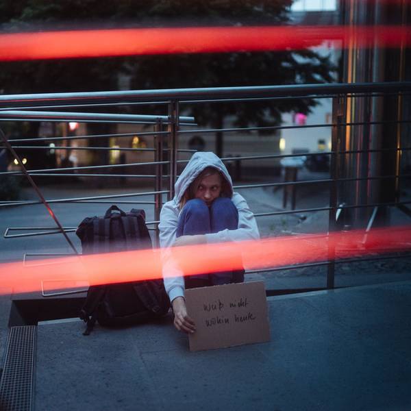 Ein Mädchen mit grauem Kapuzenpullover lehnt in der Nacht an der Gatter eines U-Bahn-Abgangs und hält ein Schild mit der Aufschrift „Weiß nicht wohin heute“ in der Hand.