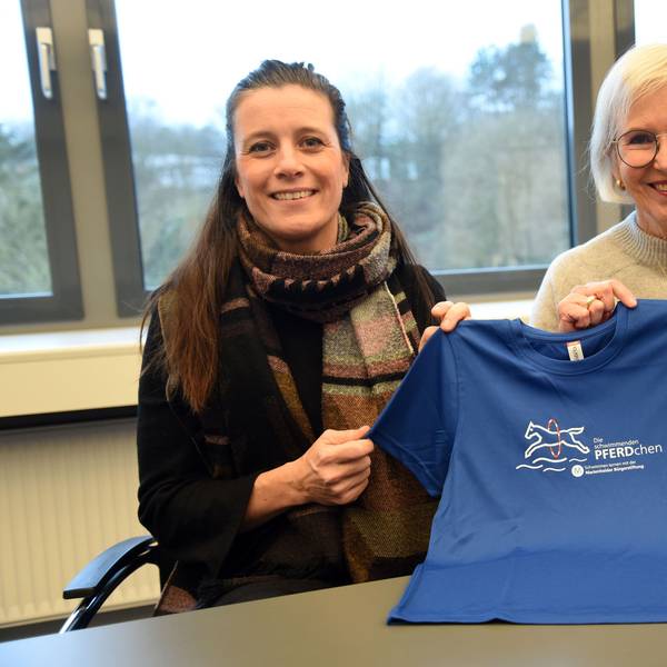 Das Foto zeigt zwei Frauen und ein blaues T-Shirt mit dem Logo des Projekts "Die schwimmenden Pferdchen".