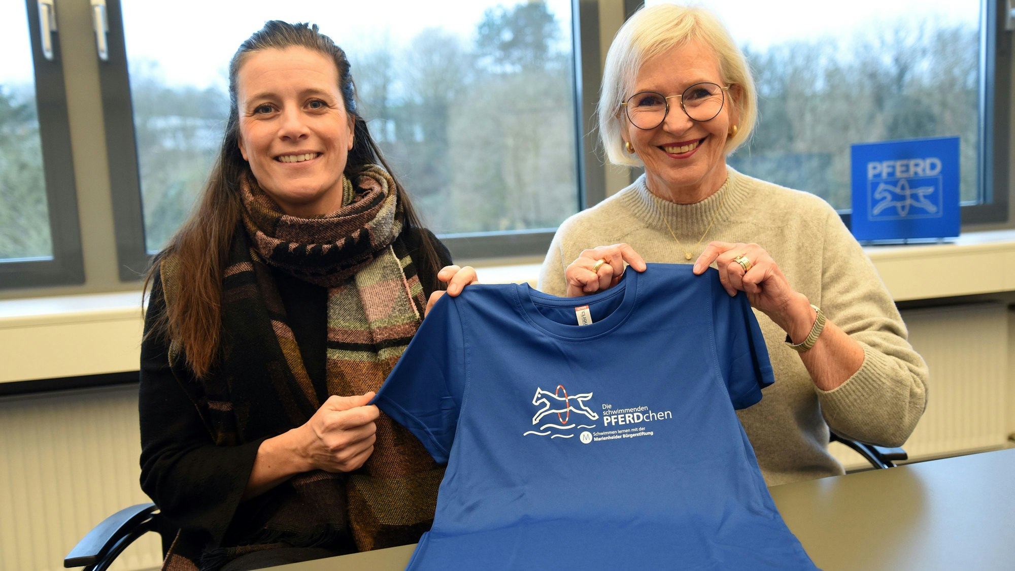 Das Foto zeigt zwei Frauen und ein blaues T-Shirt mit dem Logo des Projekts "Die schwimmenden Pferdchen".