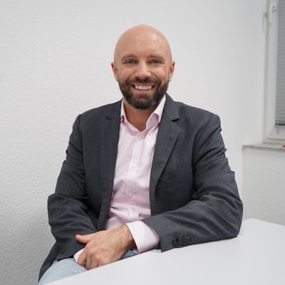 Das Foto zeigt einen Mann vor einer weißen Wand.