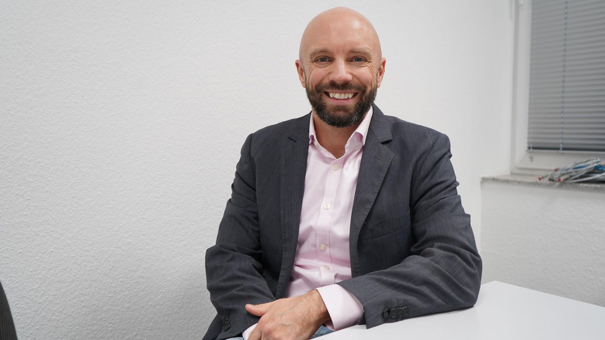 Das Foto zeigt einen Mann vor einer weißen Wand.