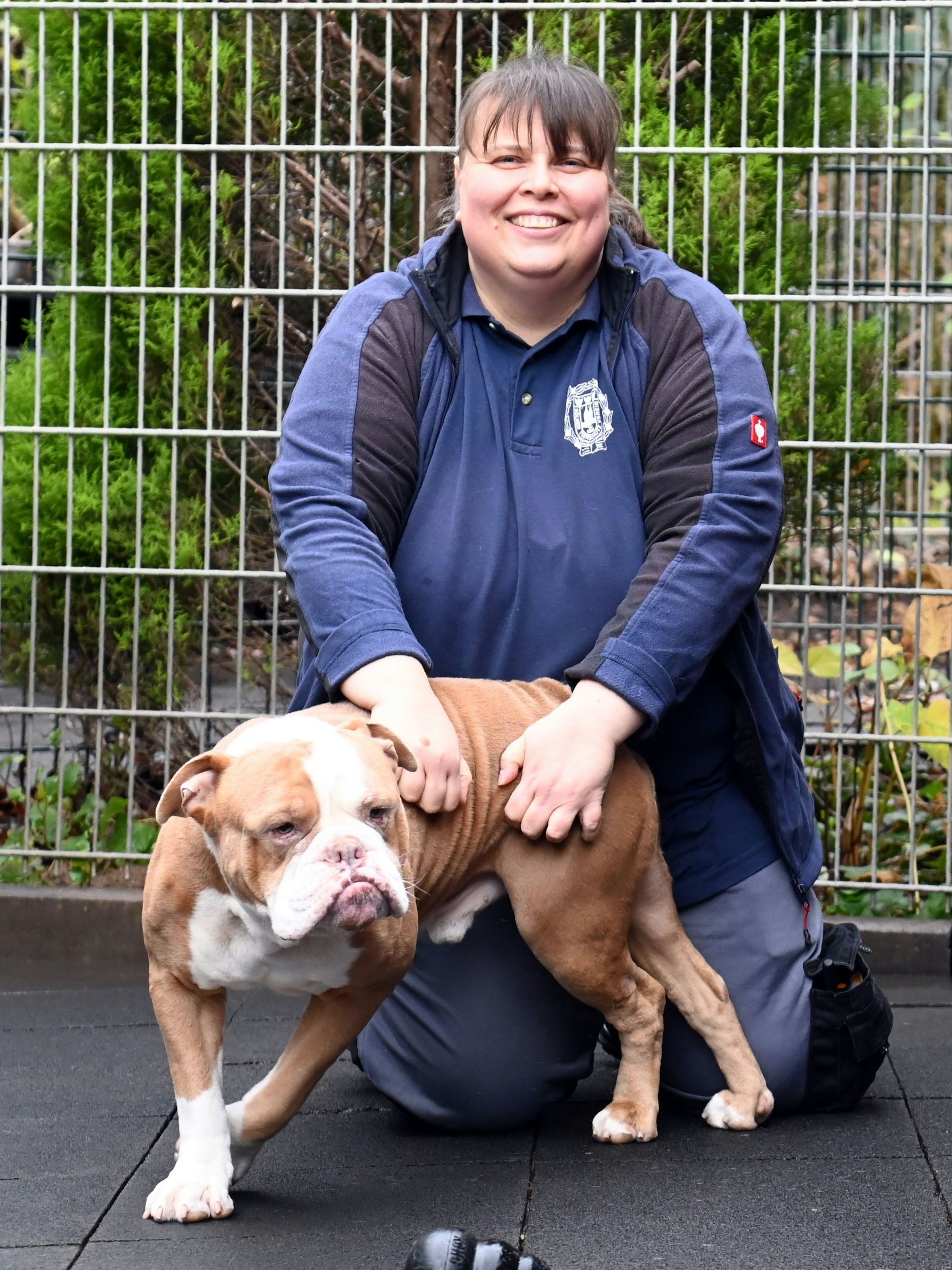 Elke Sans kniet neben der Olde English Bulldogge namens Bacon und krault ihn.