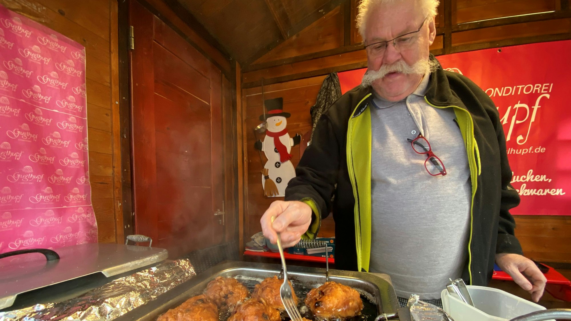 Zu sehen ist ein Verkäufer, der Krapfen frittiert.