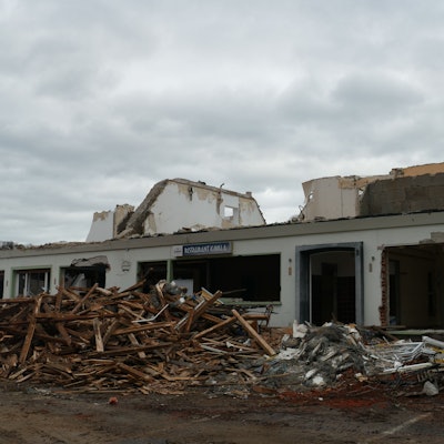 Ein Bagger an einem halb abgerissenen Haus, Balken und Schutt liegen davor.