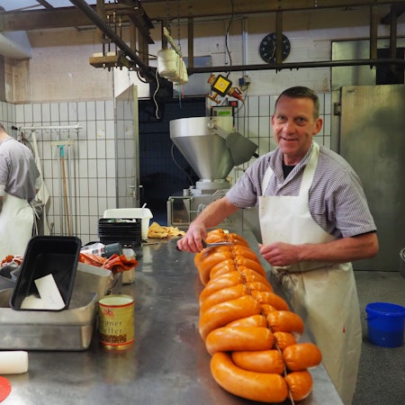 Ein Metzgermeister füllt Wurstmasse in den Darm und formt perfekte Ringe daraus.