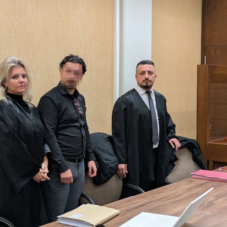 Ein Angeklagter steht zwischen seinen Rechtsanwälten in einem Saal des Kölner Landgerichts