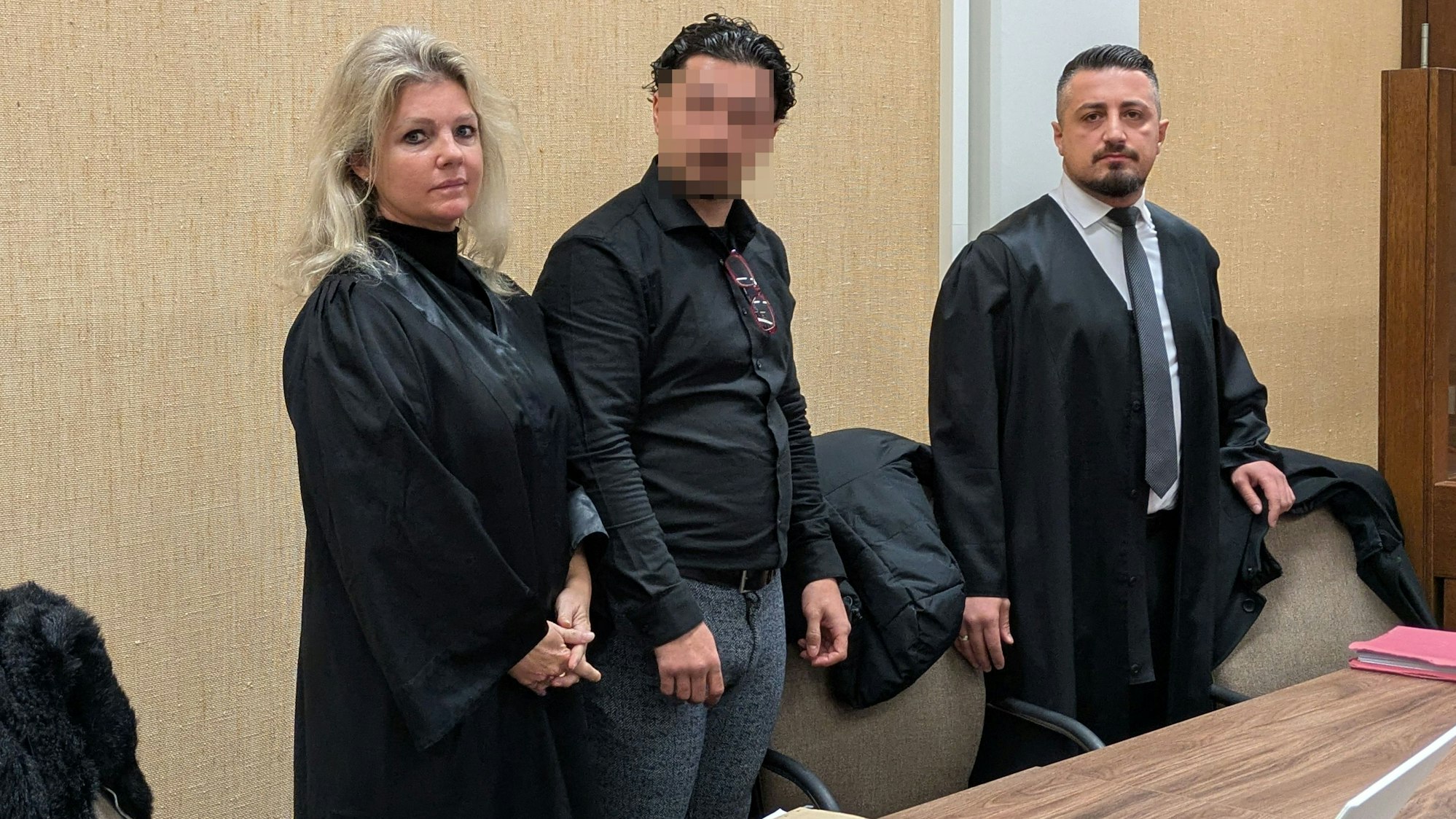 Ein Angeklagter steht zwischen seinen Rechtsanwälten in einem Saal des Kölner Landgerichts