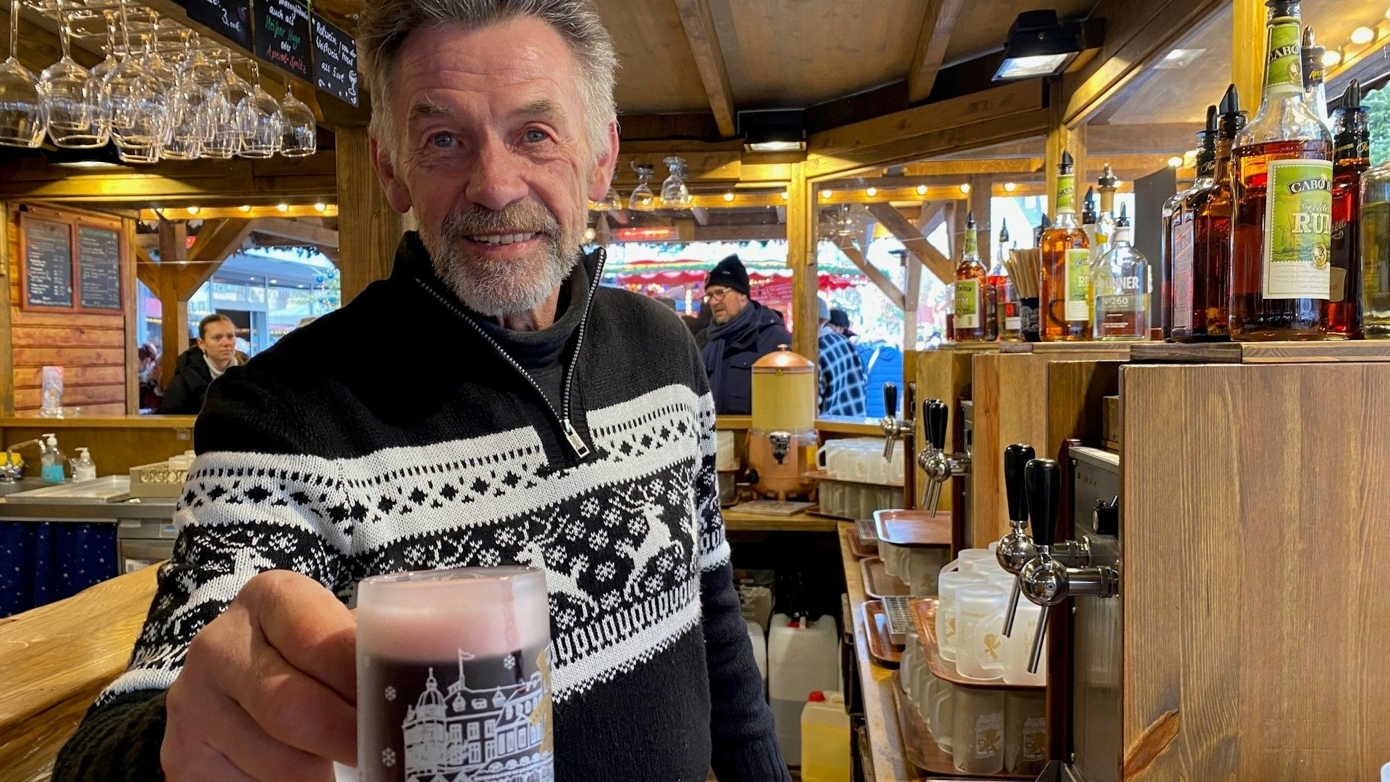 Zu sehen ist ein Verkäufer, der ein Glas Glühwein in der Hand hält.
