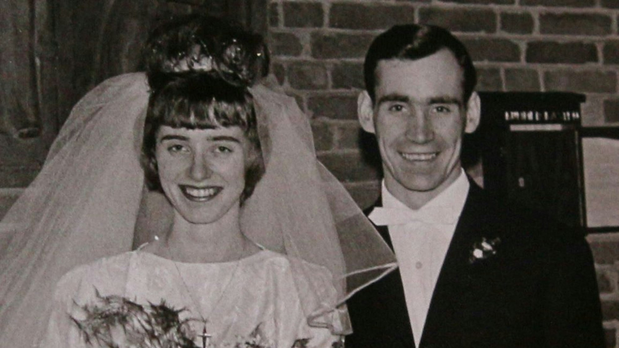 Das Ehepaar nach der kirchlichen Hochzeit, sie in einem weißen Kleid, sie trägt einen Schleier, er einen Anzug.