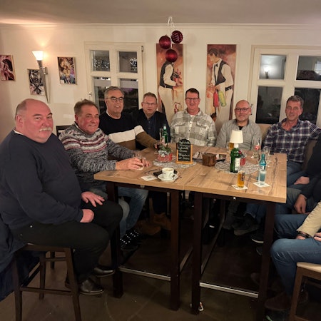 Eine Gruppe von zehn Männern sitzt um den Tisch einer Kneipe.